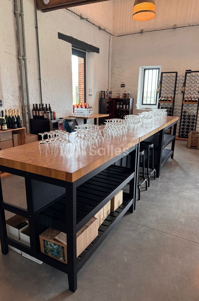 Salle de dégustation avec un long comptoir en bois, verres alignés, bouteilles et casiers à vin en arrière-plan.