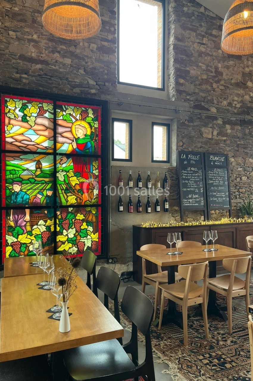 Salle de restaurant avec tables en bois, vitrail coloré, étagère de bouteilles de vin et ardoises de menu au mur.