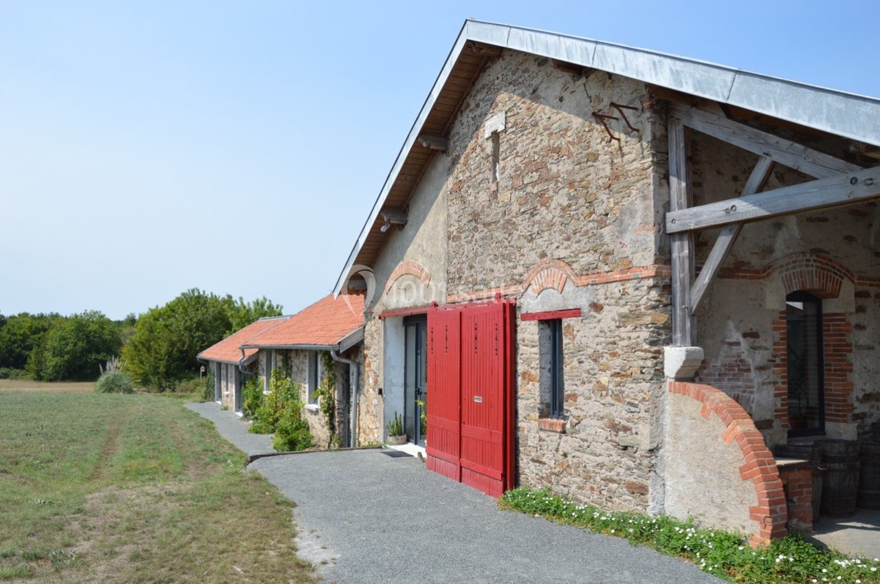 Bâtiment en pierre avec portes rouges, toit en tuiles et poutres en bois, entouré de végétation et d'un chemin pavé.