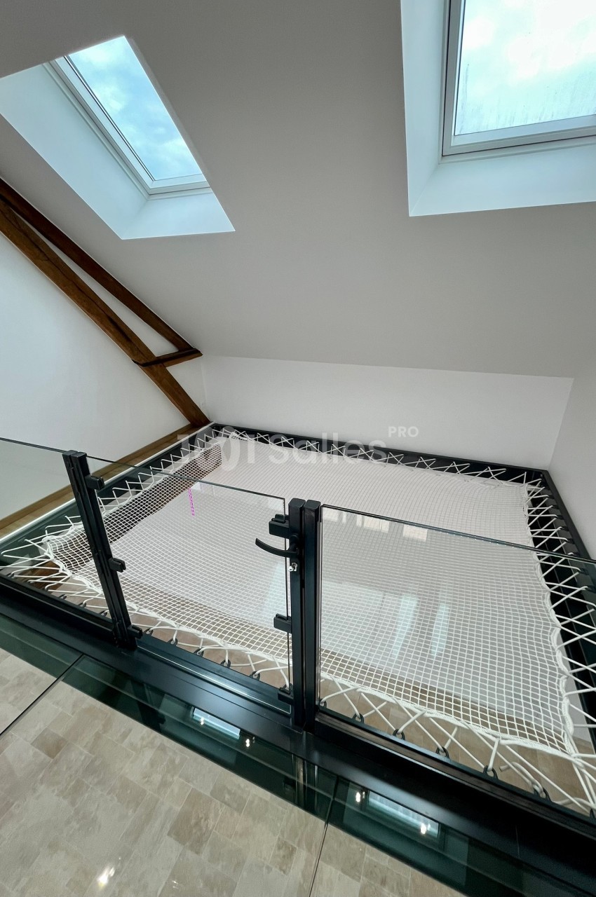Filet suspendu installé dans un espace mezzanine lumineux avec garde-corps en verre et fenêtres de toit.