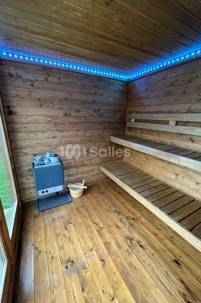 Intérieur d'un sauna en bois avec bancs, poêle à pierres et éclairage LED bleu au plafond.