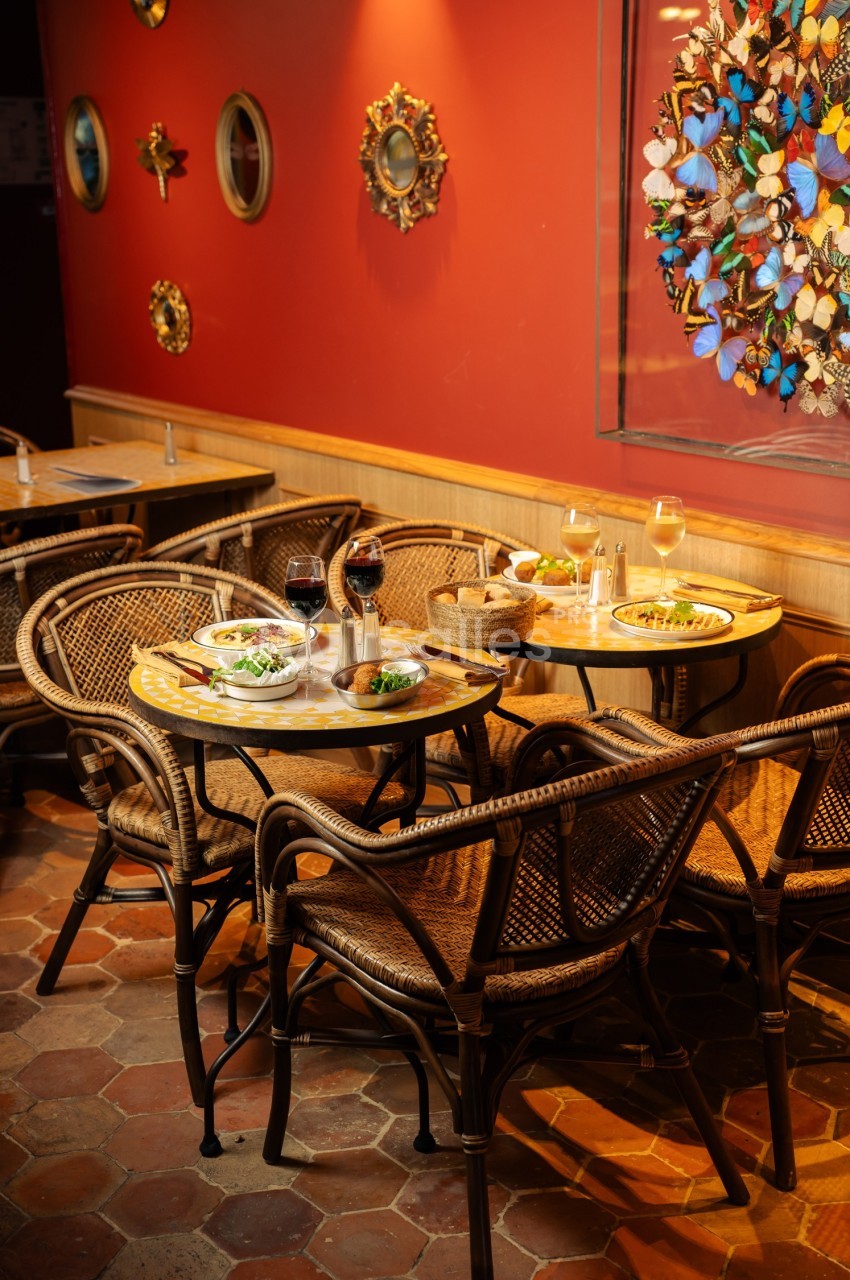 Tables en rotin dressées avec des assiettes et des verres de vin dans un restaurant à la décoration murale colorée.