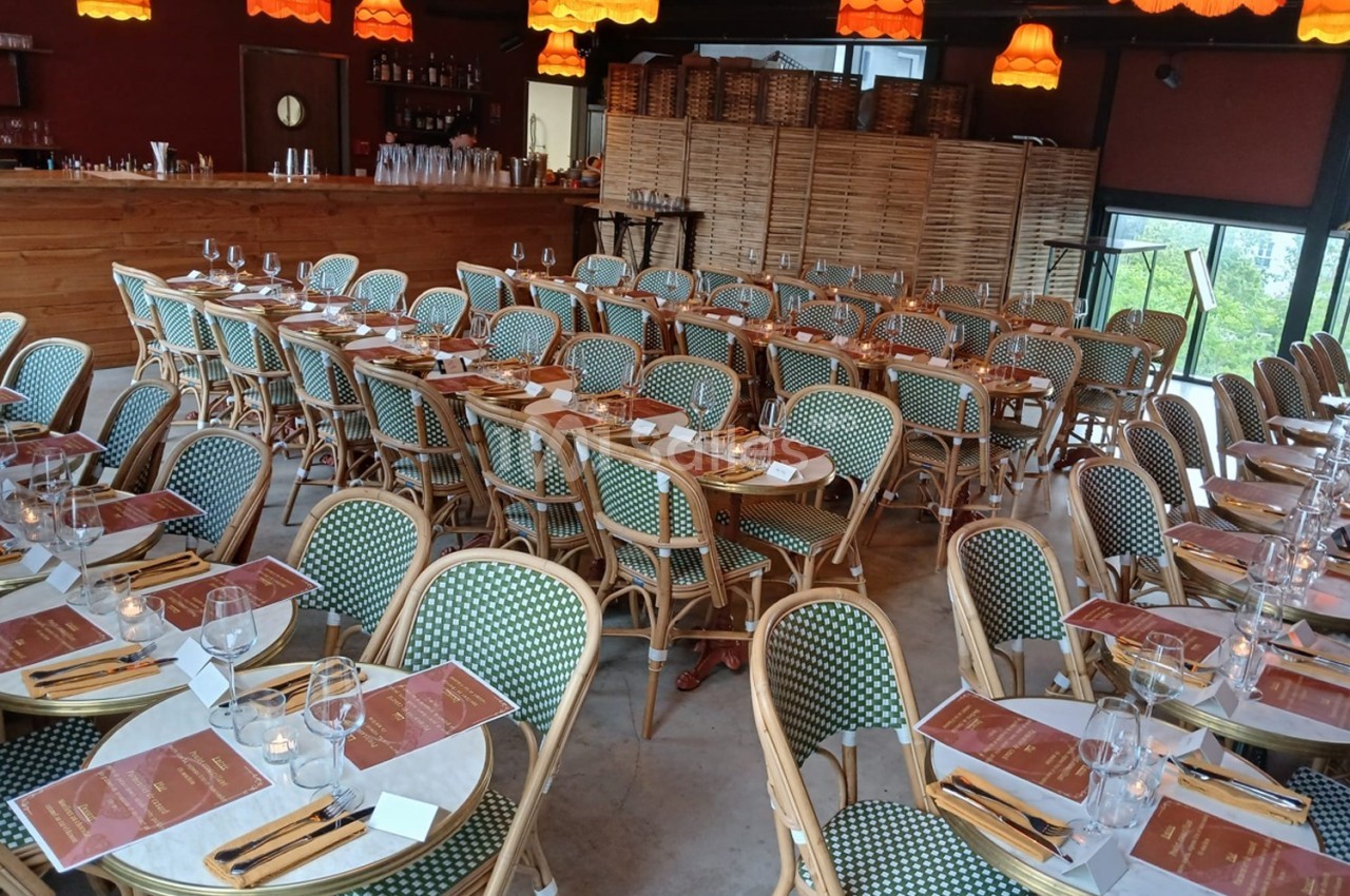 Salle de restaurant avec tables dressées, chaises en osier et lampes suspendues orange dans une ambiance chaleureuse.