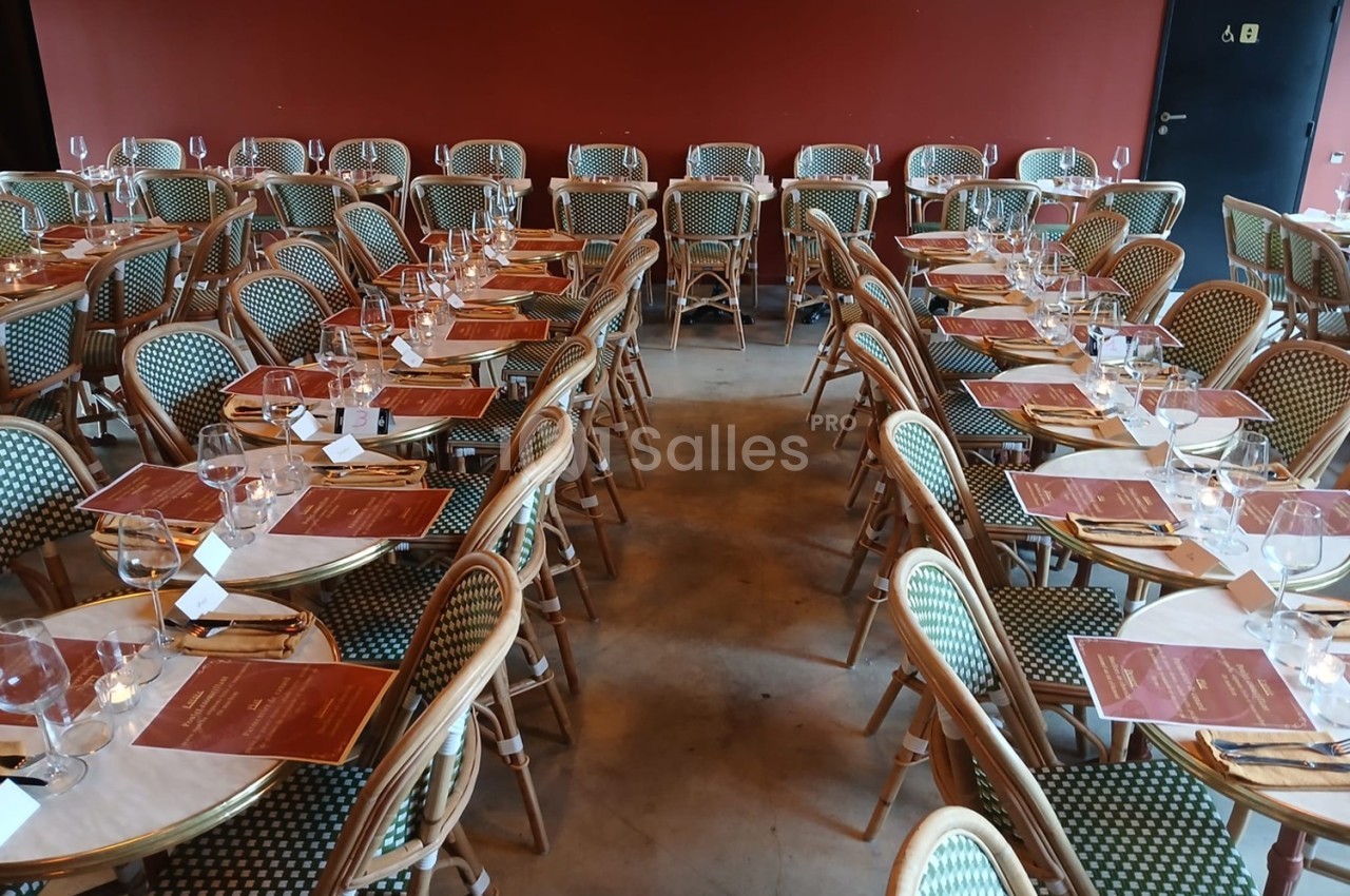 Salle de restaurant avec des tables dressées, alignées, couvertes de nappes blanches, menus et verres à vin.
