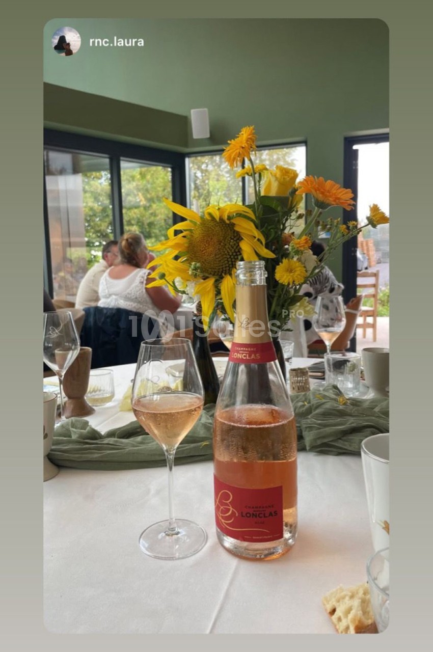 Bouteille de vin rosé et verre servis sur une table dressée avec des fleurs jaunes en arrière-plan lumineux.