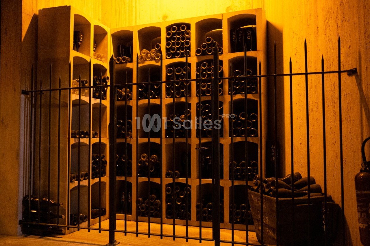 Casiers en bois remplis de bouteilles de vin, éclairés par une lumière chaude, derrière une grille métallique.