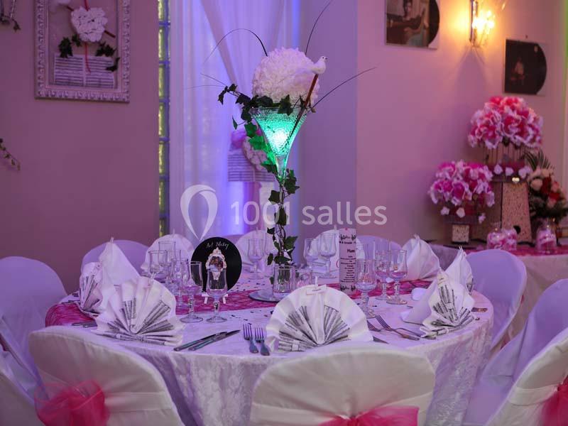 Table de réception décorée avec nappes blanches, serviettes pliées, verres, et centre de table floral lumineux.