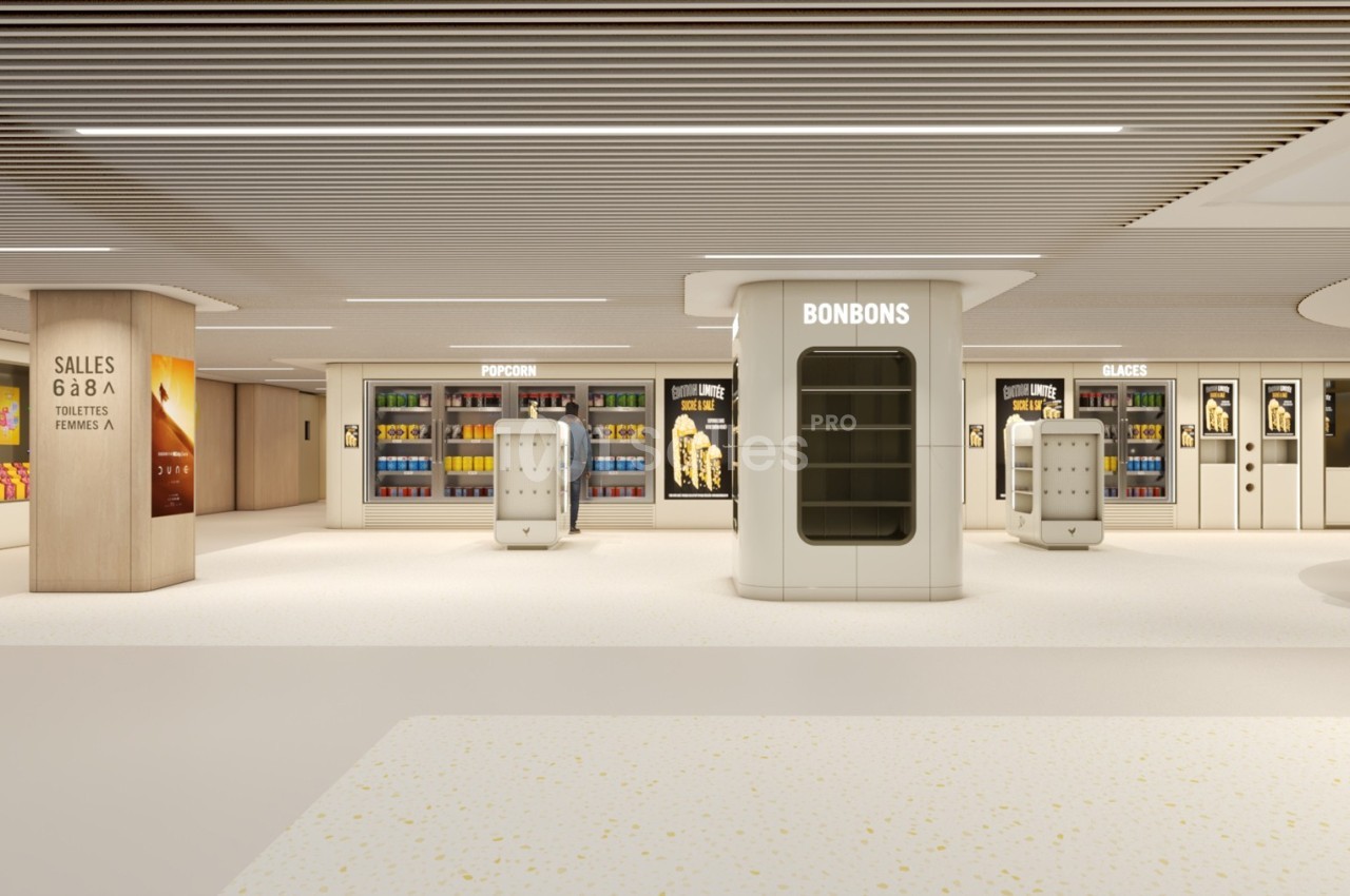 Vue d'un espace de vente moderne avec rayons de bonbons, pop-corn et glaces dans un hall lumineux.