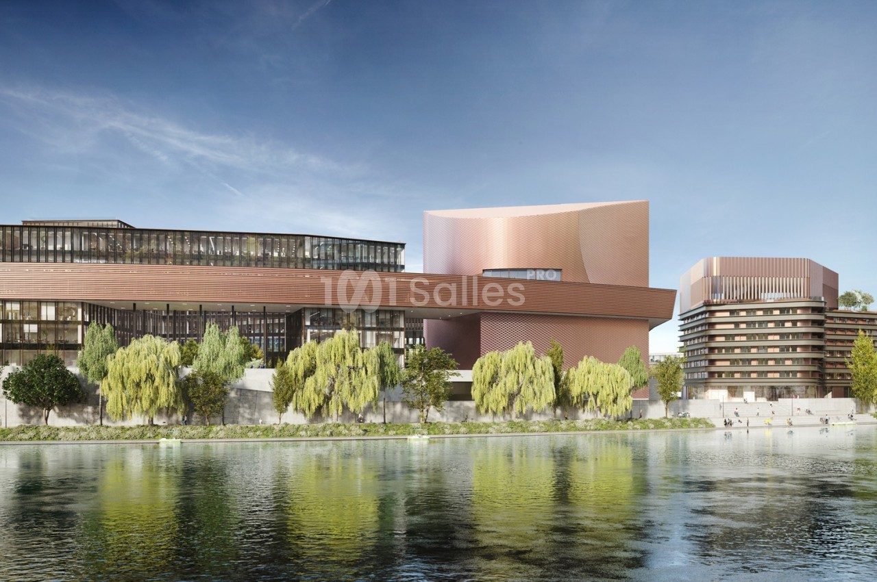 Vue d'un complexe architectural moderne en bord de rivière, entouré d'arbres et reflété dans l'eau calme.