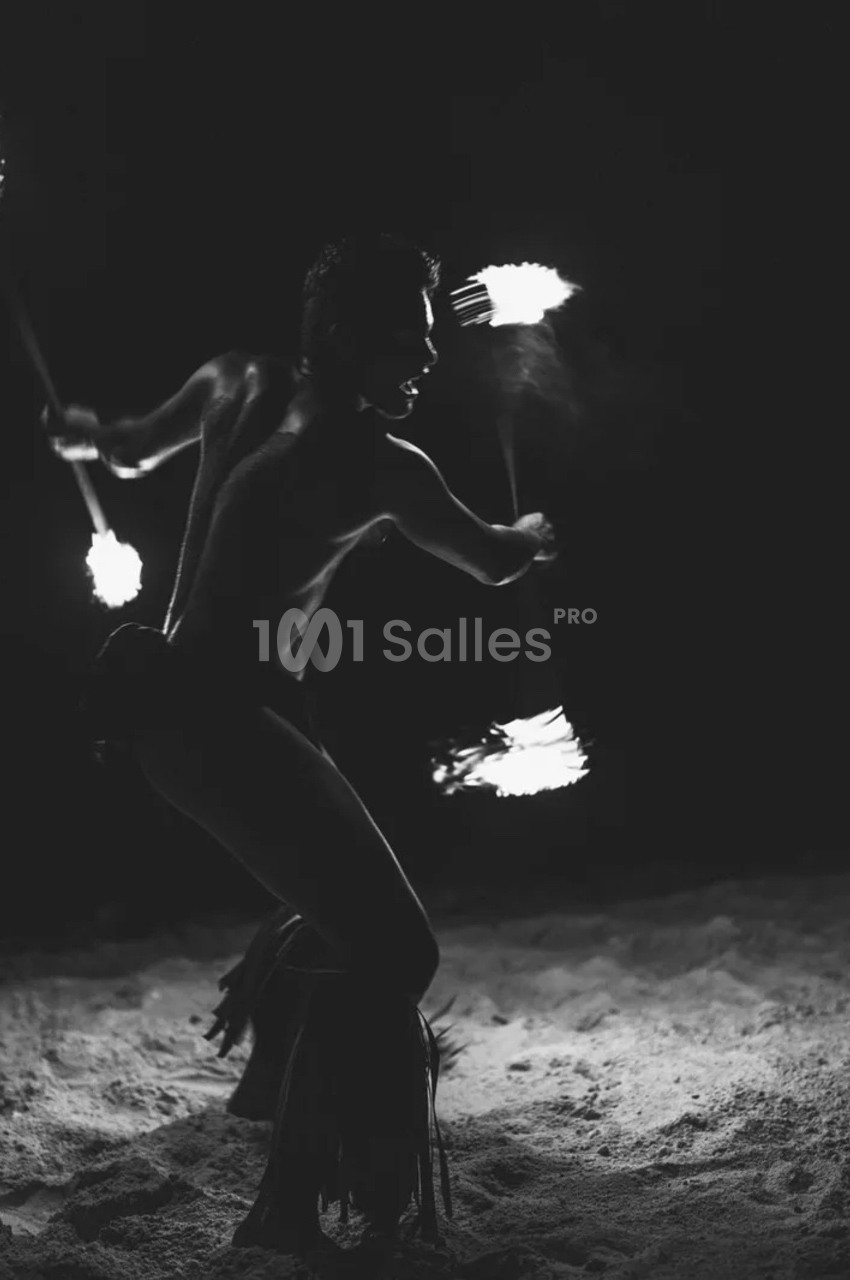 Un artiste jongle avec des torches enflammées dans l'obscurité, sur un sol sablonneux.