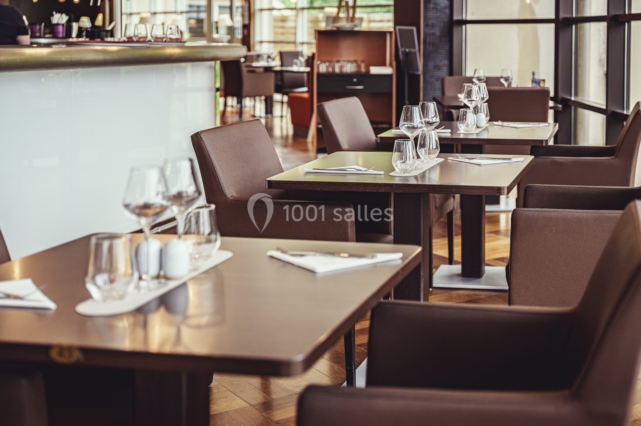 Tables de restaurant élégantes avec chaises en cuir, verres et serviettes disposés dans un intérieur moderne et lumineux.