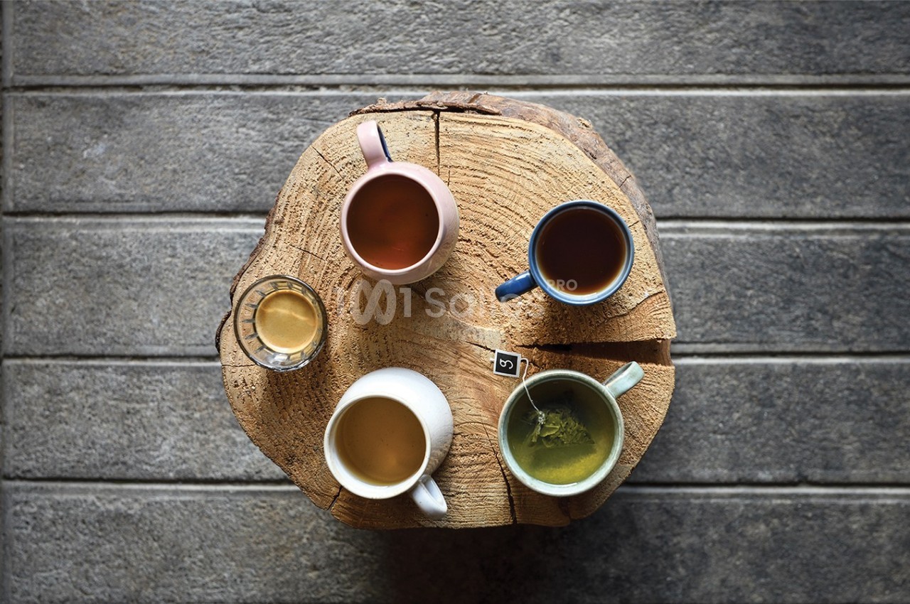 Quatre boissons chaudes variées servies dans des tasses colorées, disposées sur une table en bois rond.