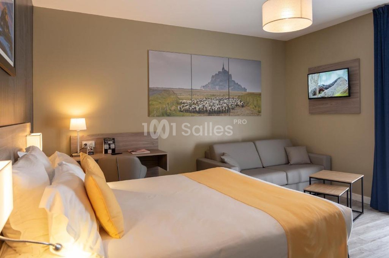 Chambre d'hôtel avec lit double, canapé, bureau, éclairage doux et décoration murale représentant des paysages.