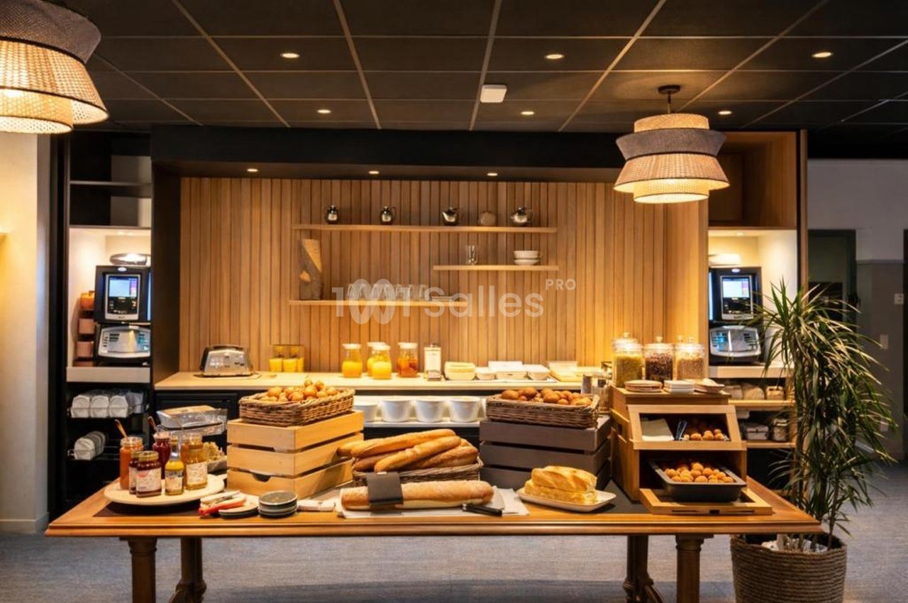 Buffet de petit-déjeuner avec pains, viennoiseries, confitures, céréales et boissons dans une salle lumineuse.