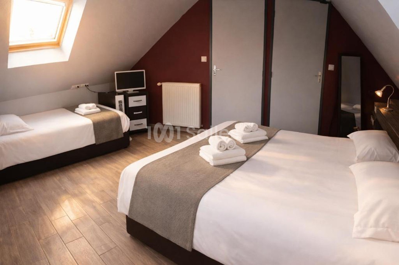 Chambre mansardée avec un lit double, un lit simple, un bureau, une télévision et une fenêtre de toit.