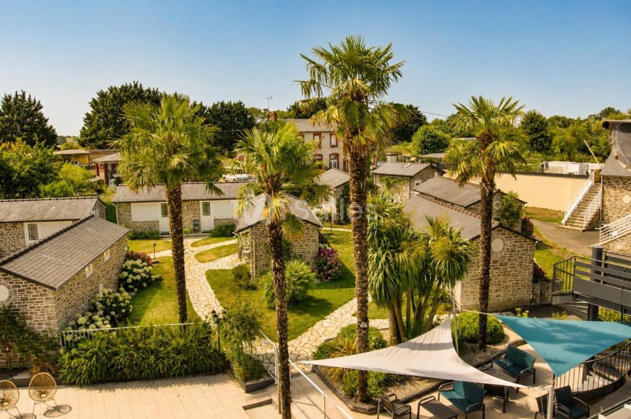 Vue d'un complexe de petites maisons en pierre entouré de palmiers et de jardins sous un ciel dégagé.