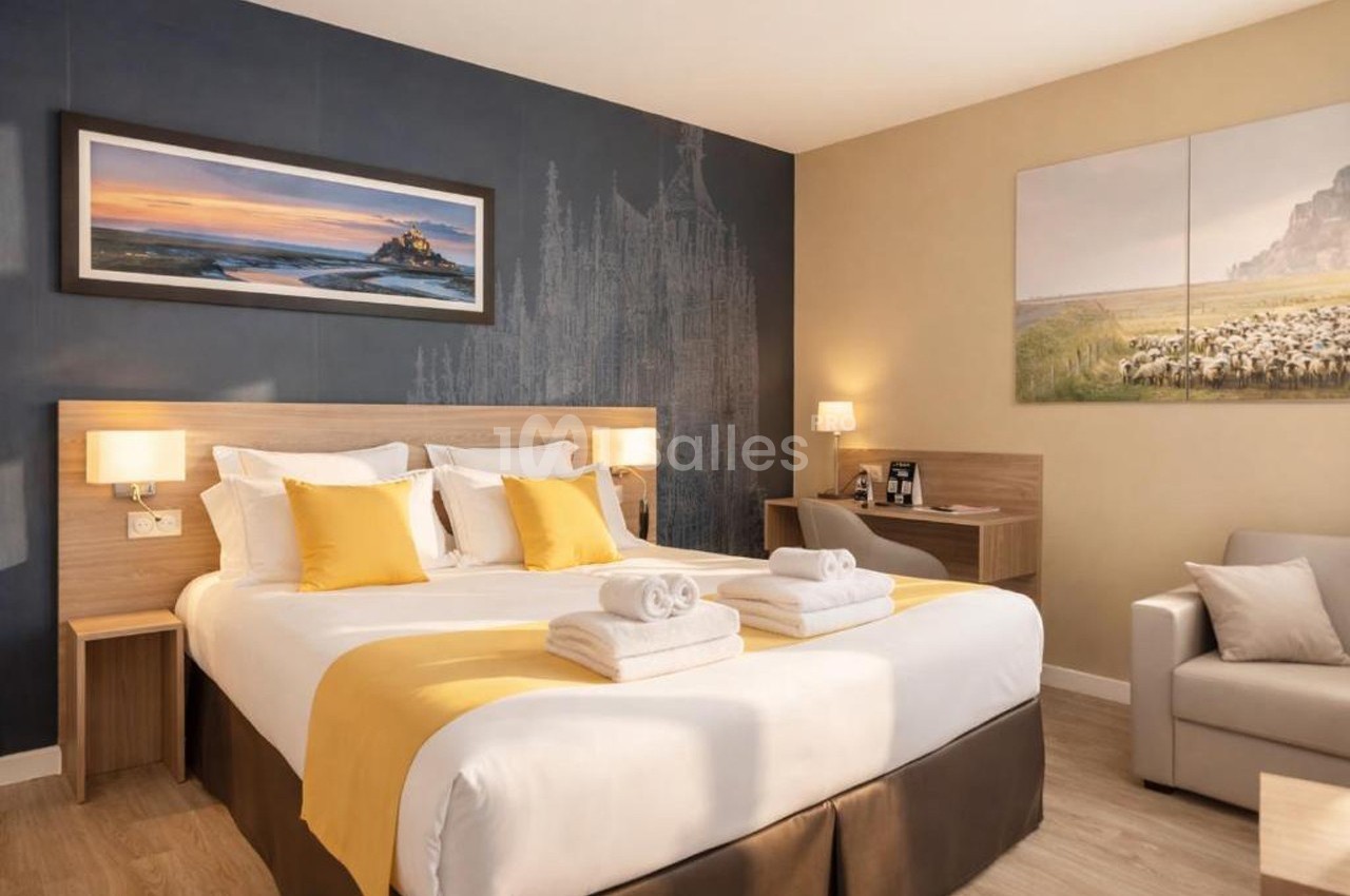 Chambre d'hôtel lumineuse avec un lit double, des coussins jaunes, un bureau, un canapé et des décorations murales.
