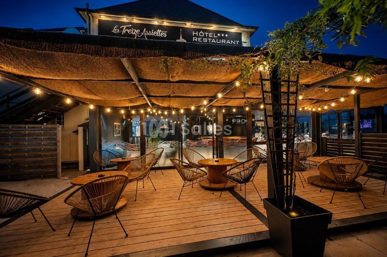 Terrasse d'un restaurant éclairée par des guirlandes lumineuses, avec des fauteuils en rotin et un toit en canisses.