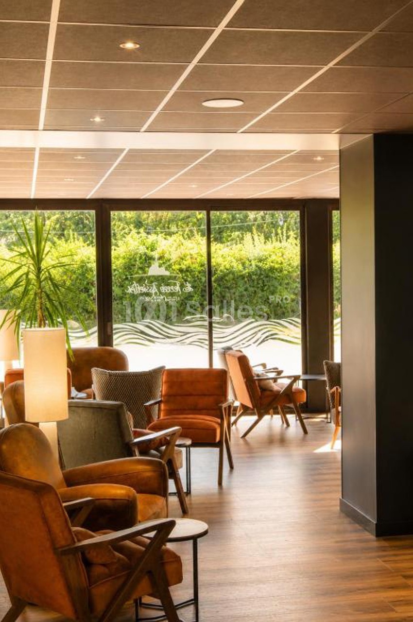 Espace lounge avec fauteuils en cuir, tables basses et grandes baies vitrées donnant sur un jardin verdoyant.