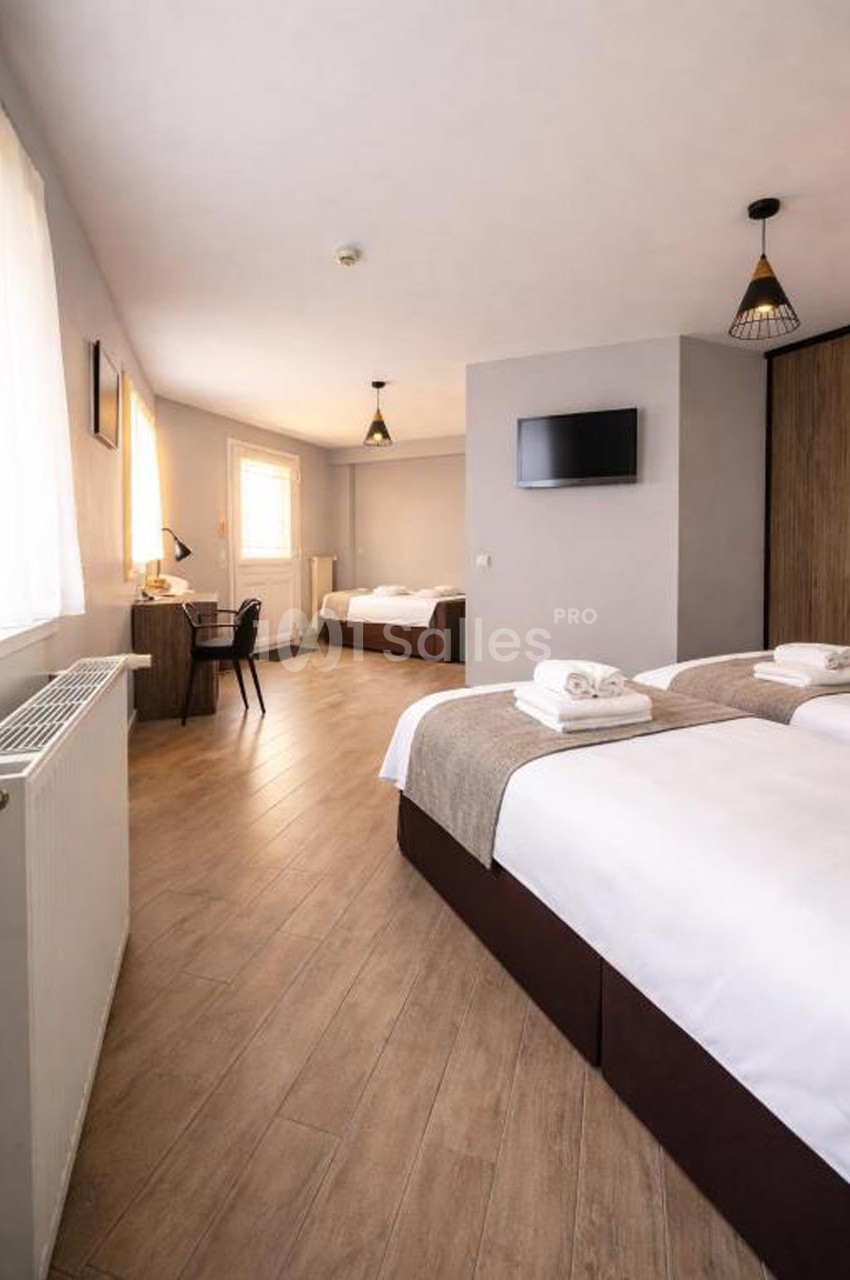 Chambre lumineuse avec deux lits doubles, un bureau, une télévision murale et un sol en parquet clair.