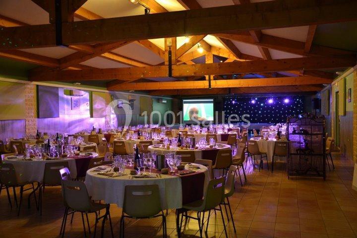 Salle de réception décorée avec des tables rondes dressées, éclairage tamisé et écran de projection en arrière-plan.