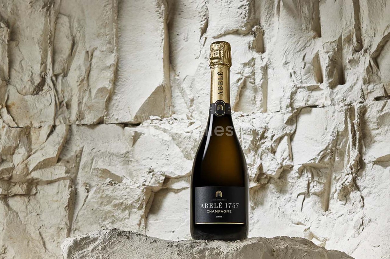 Bouteille de champagne Abelé 1757 posée sur un rocher devant un mur de pierre blanche.