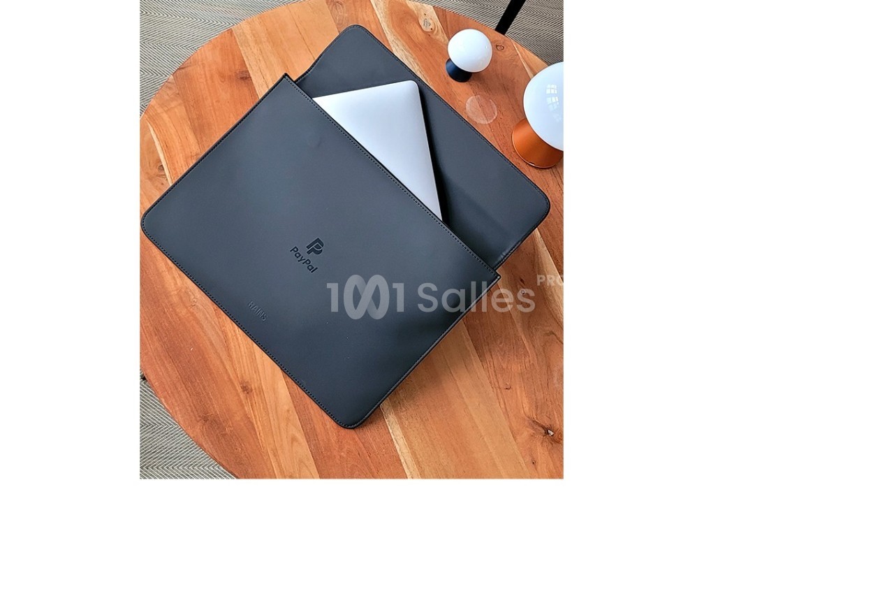 Ordinateur portable partiellement glissé dans une pochette noire posée sur une table en bois.