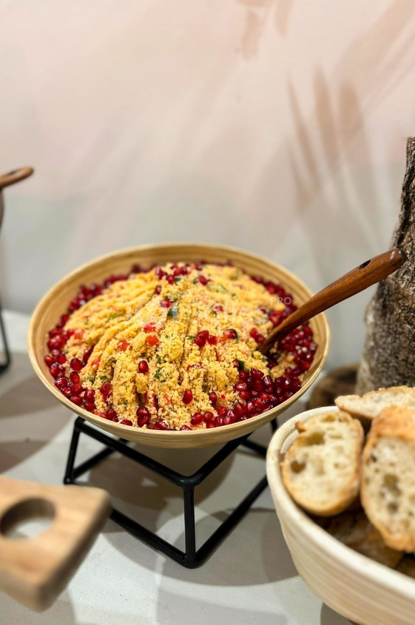 Salade de couscous garnie de graines de grenade dans un bol en bois, accompagnée de tranches de pain.