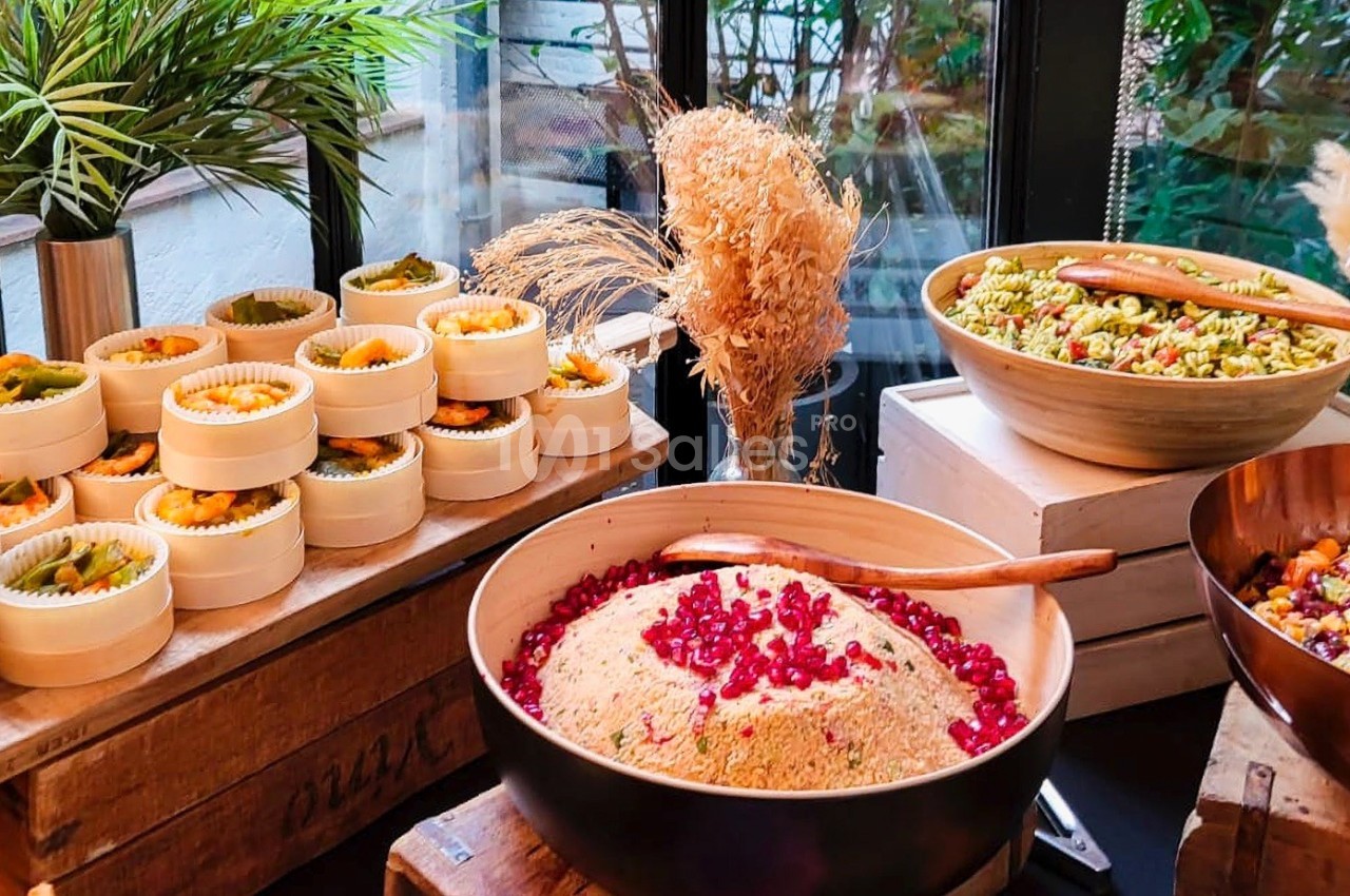 Buffet avec salades variées, couscous aux grenades et plats colorés, présenté sur des tables en bois près d'une fenêtre.