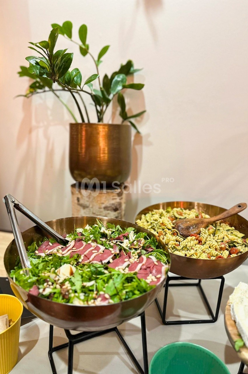 Deux saladiers en métal contenant une salade verte et une salade de pâtes, posés sur des supports devant une plante.