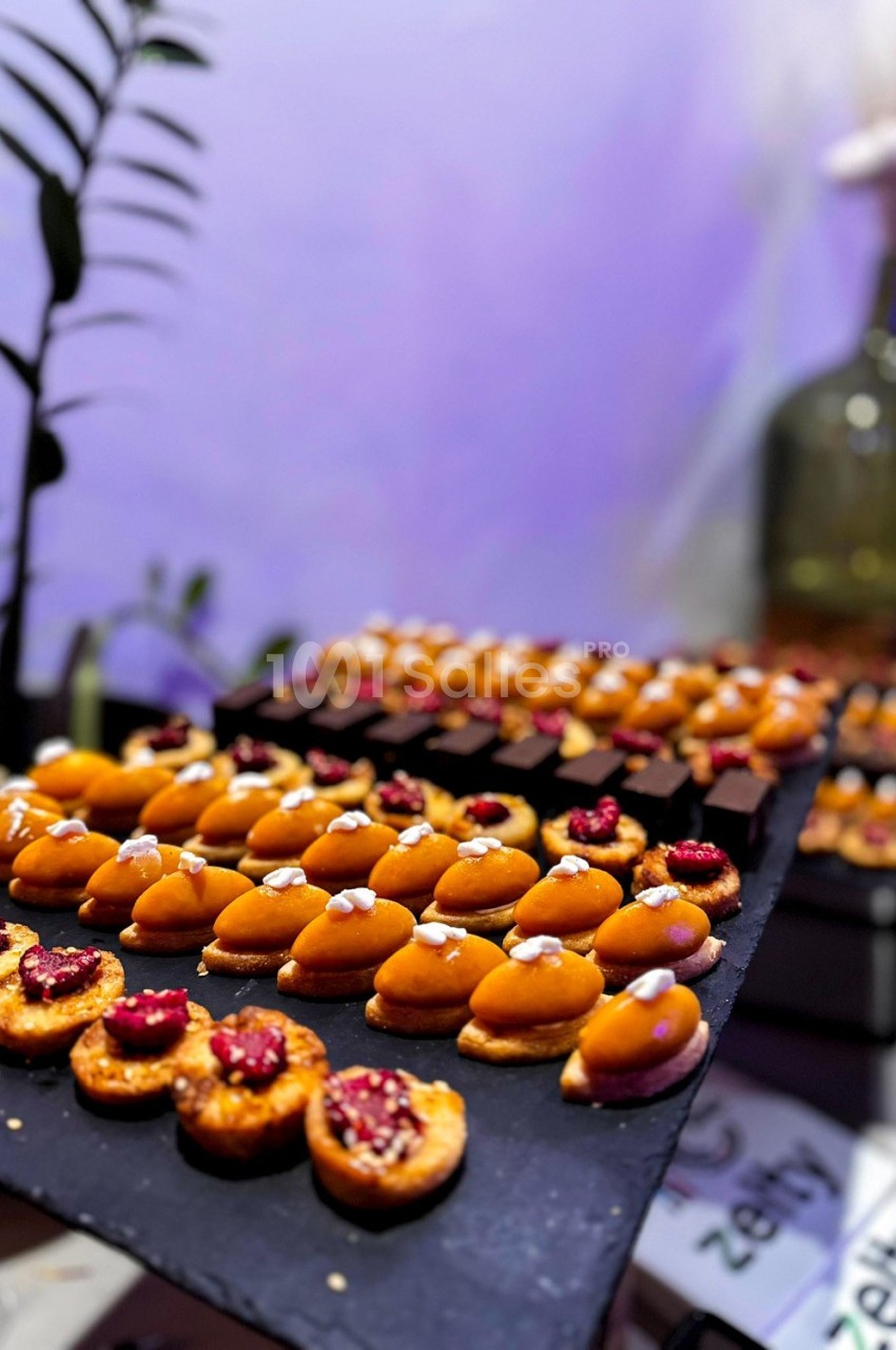 Plateau de mignardises variées, comprenant des tartelettes aux fruits et des bouchées sucrées, présenté sur une ardoise.