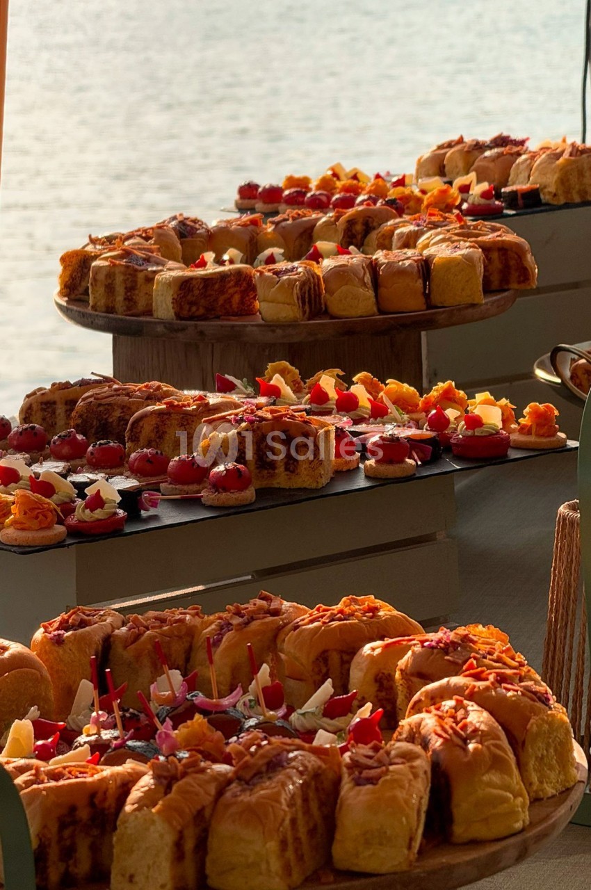Plateaux de viennoiseries et pâtisseries variées disposés sur une table avec vue sur l'eau en arrière-plan.