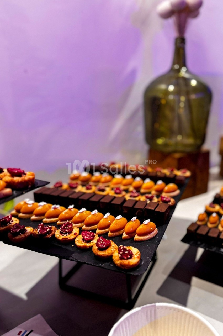 Plateaux de mignardises variées, incluant des chocolats et des pâtisseries fruitées, présentés sur des supports noirs.