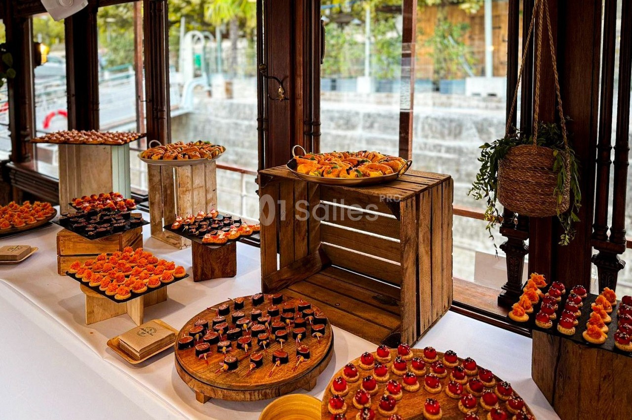 Buffet de petits fours variés disposés sur des présentoirs en bois près de grandes fenêtres donnant sur l'extérieur.