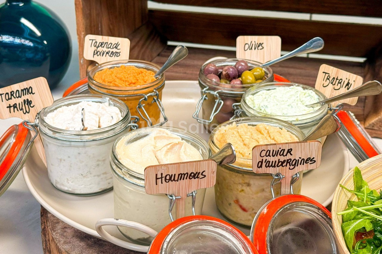 Plateau de tartinades variées en pots, incluant houmous, tarama, tapenade et tzatziki, accompagnées d'olives.