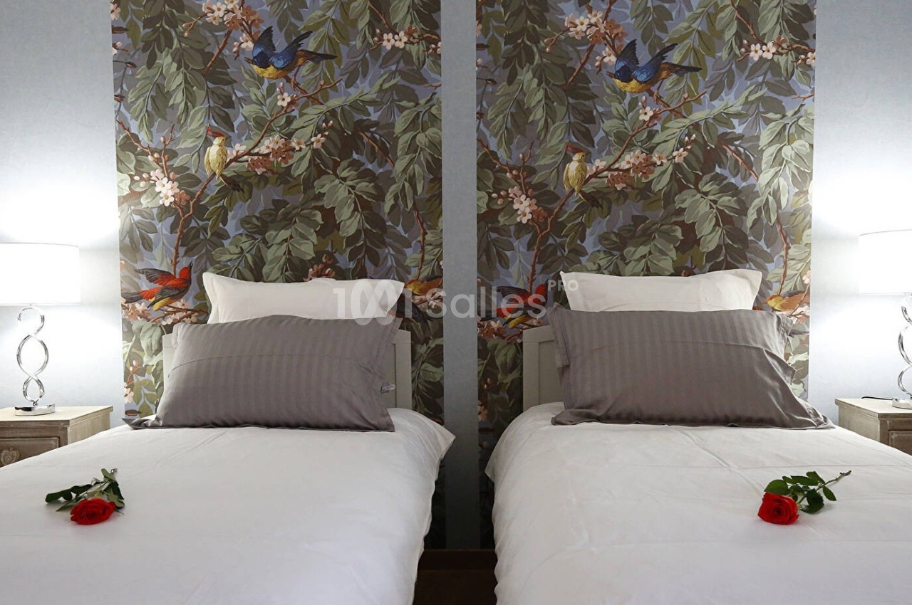 Deux lits simples avec linge blanc, coussins gris, roses rouges sur chaque lit et lampes allumées de chaque côté.