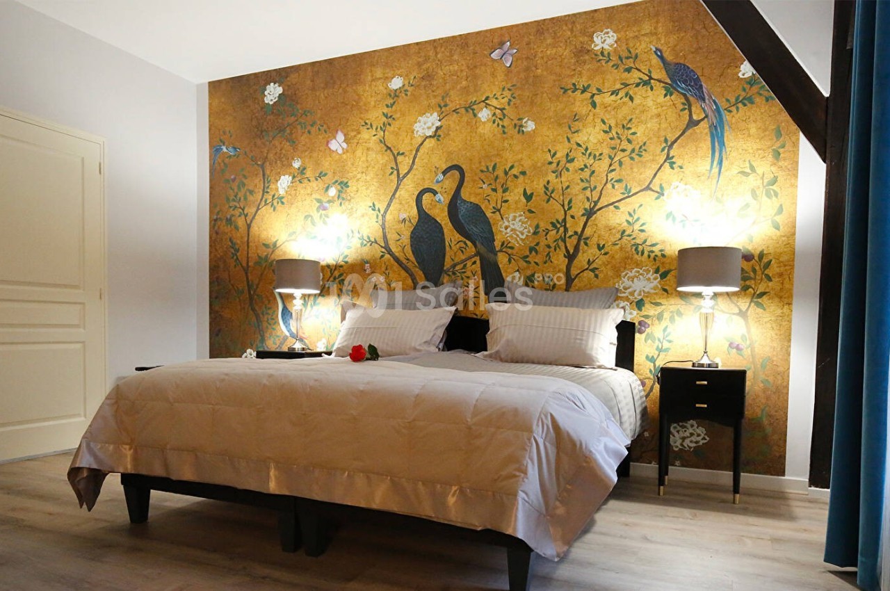 Chambre avec un lit double, mur décoré d'une fresque dorée avec des oiseaux, éclairée par deux lampes de chevet.