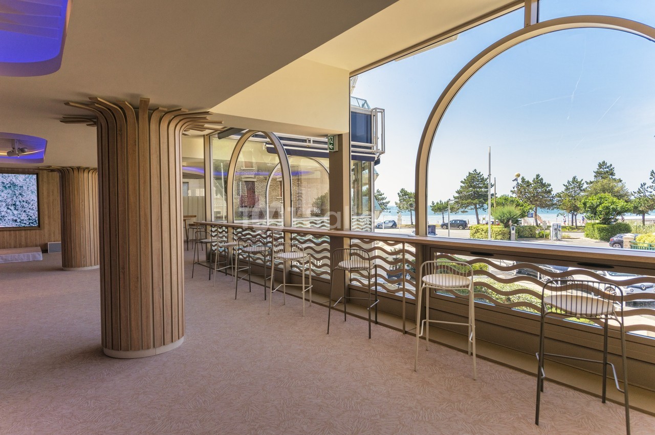 Salle lumineuse avec de grandes baies vitrées donnant sur un paysage arboré et des chaises alignées le long d'un comptoir.
