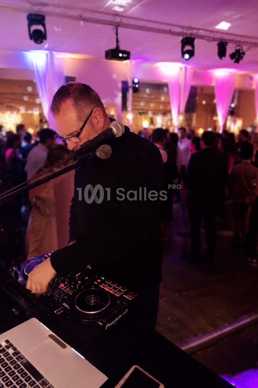 Un DJ mixant de la musique lors d'une soirée festive avec des invités dans une salle éclairée par des lumières colorées.