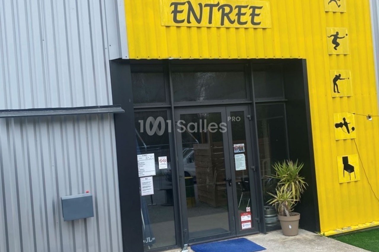 Entrée d'un bâtiment avec une façade jaune et grise, signalée par un panneau ’ENTREE’ et des pictogrammes sportifs.