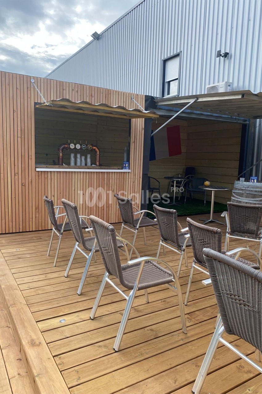 Terrasse en bois avec des chaises en rotin face à un comptoir de bar extérieur sous un auvent.