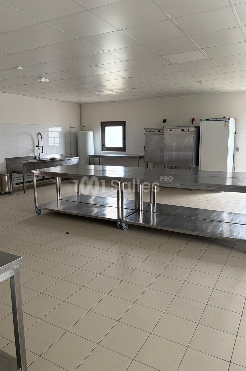 Cuisine professionnelle avec plans de travail en inox, équipements de cuisson et carrelage au sol beige.