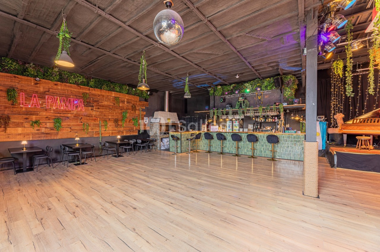 Salle spacieuse avec bar en bambou, tables, décor végétal, enseigne lumineuse ’La Pampa’ et boule disco au plafond.