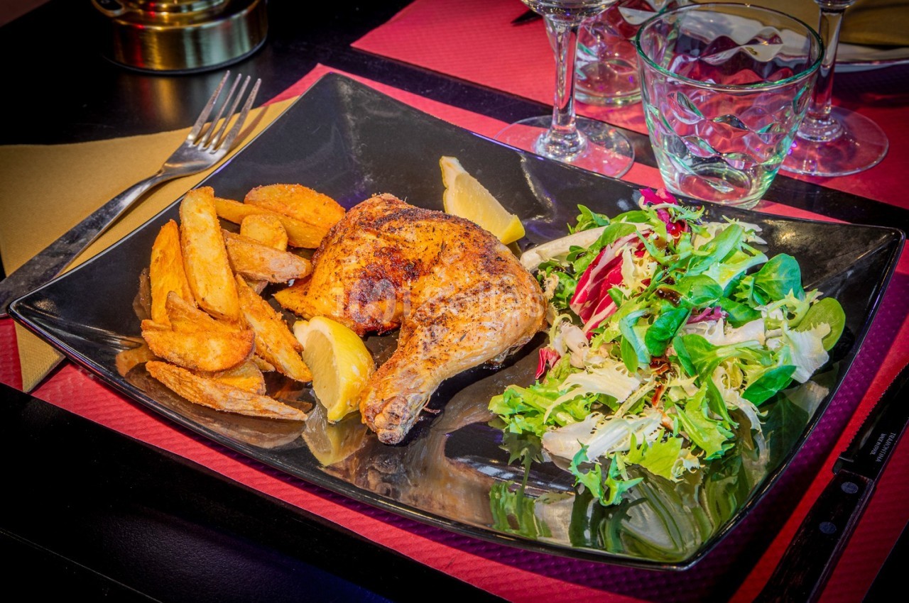 Assiette contenant un morceau de poulet rôti, des pommes de terre rôties et une salade verte sur une table dressée.