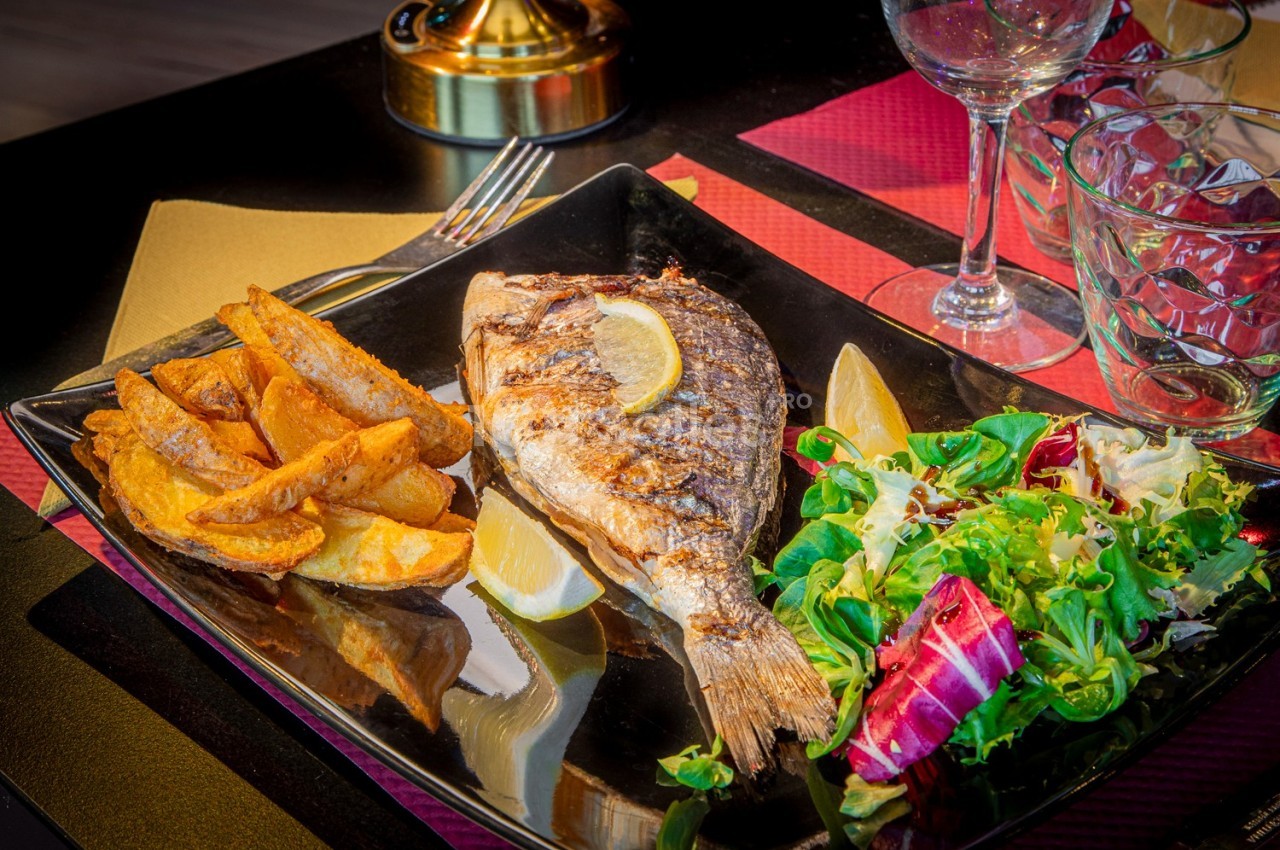 Assiette avec un poisson grillé, des quartiers de pommes de terre, une salade verte et des tranches de citron.