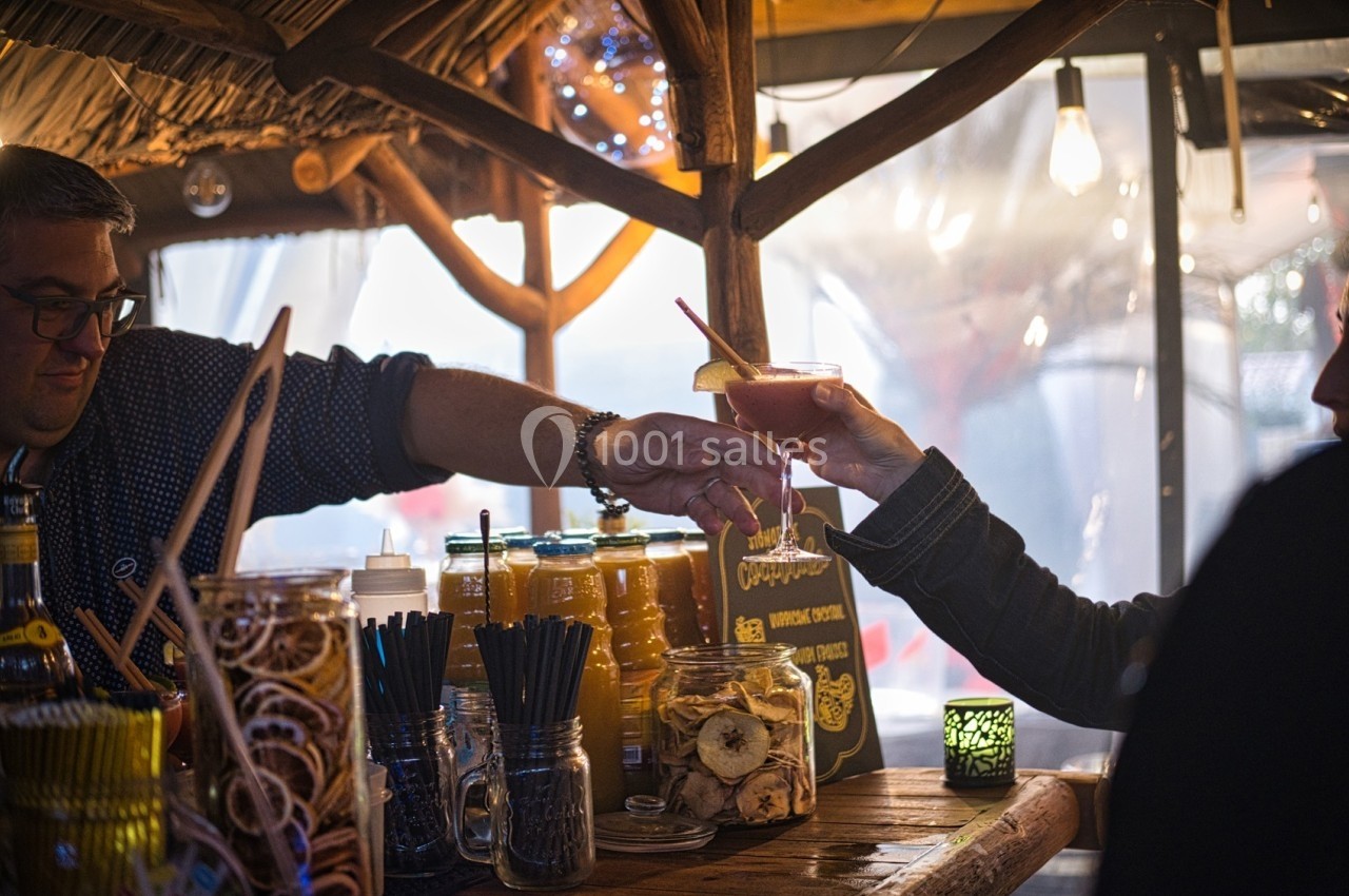 Un serveur tend un cocktail à un client dans un bar en bois à l'ambiance chaleureuse et éclairage tamisé.