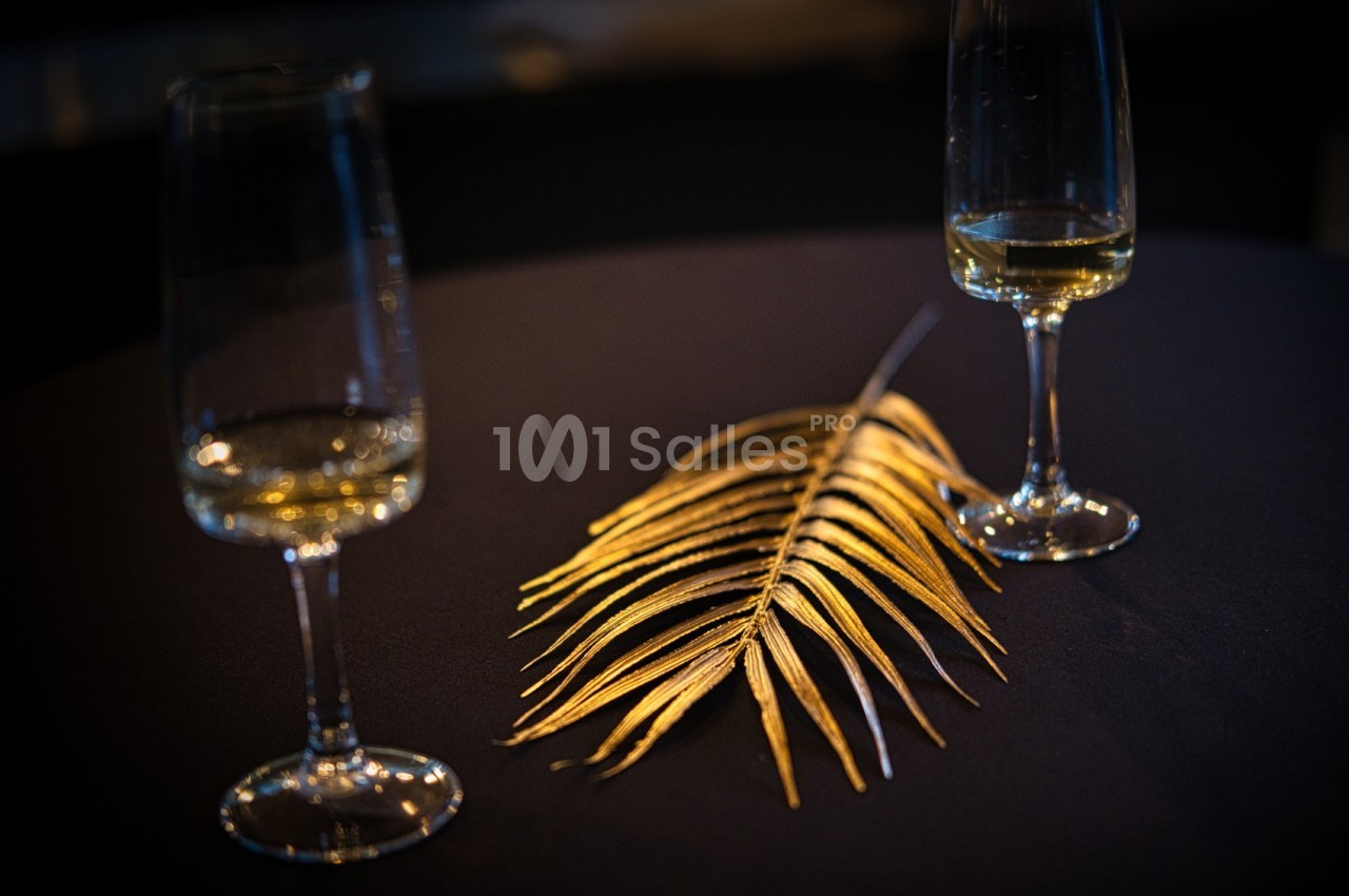 Deux verres à pied partiellement remplis entourent une feuille dorée posée sur une table sombre.