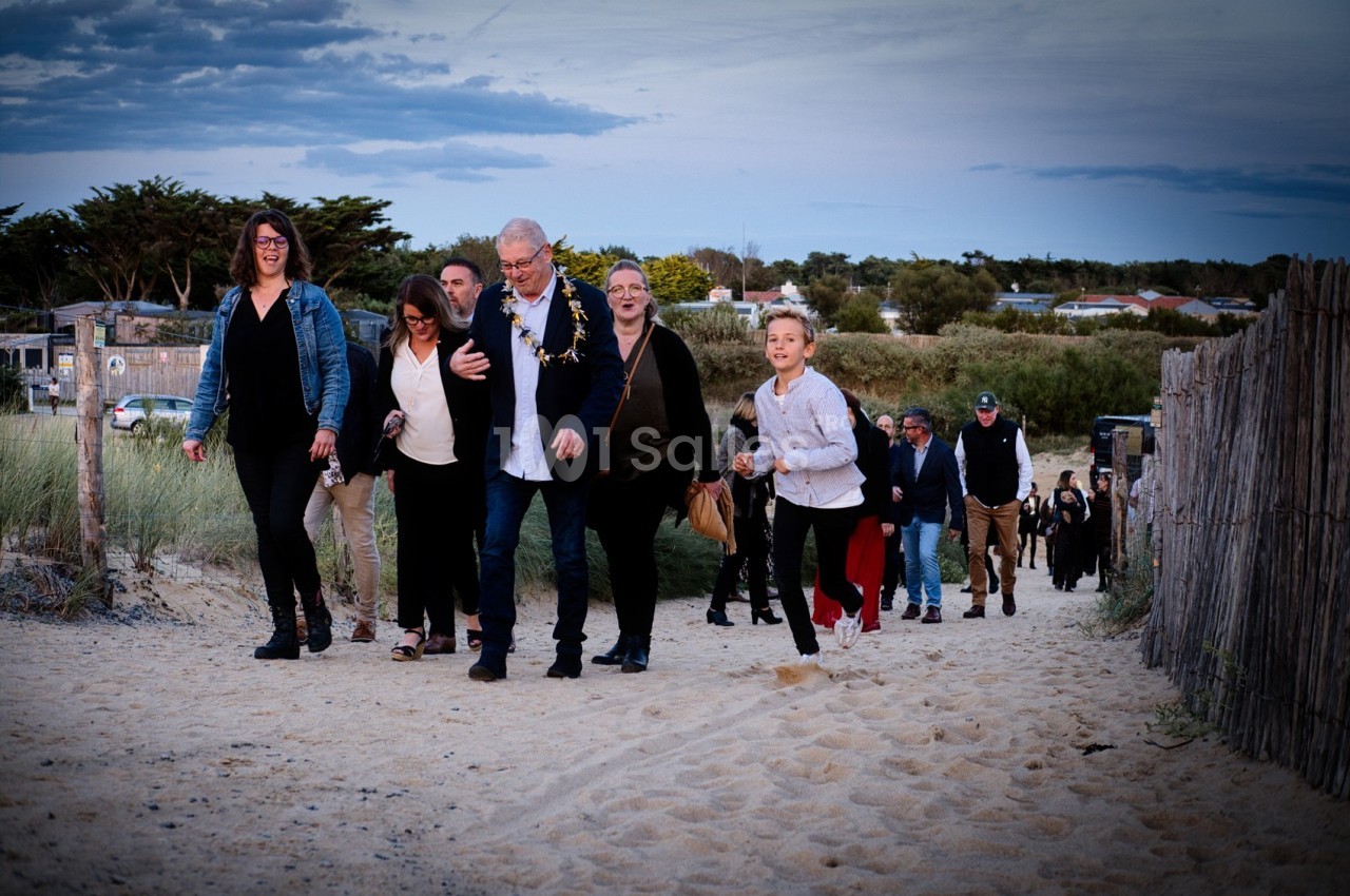 Un groupe de personnes marche sur un sentier sablonneux entouré de dunes et de végétation.
