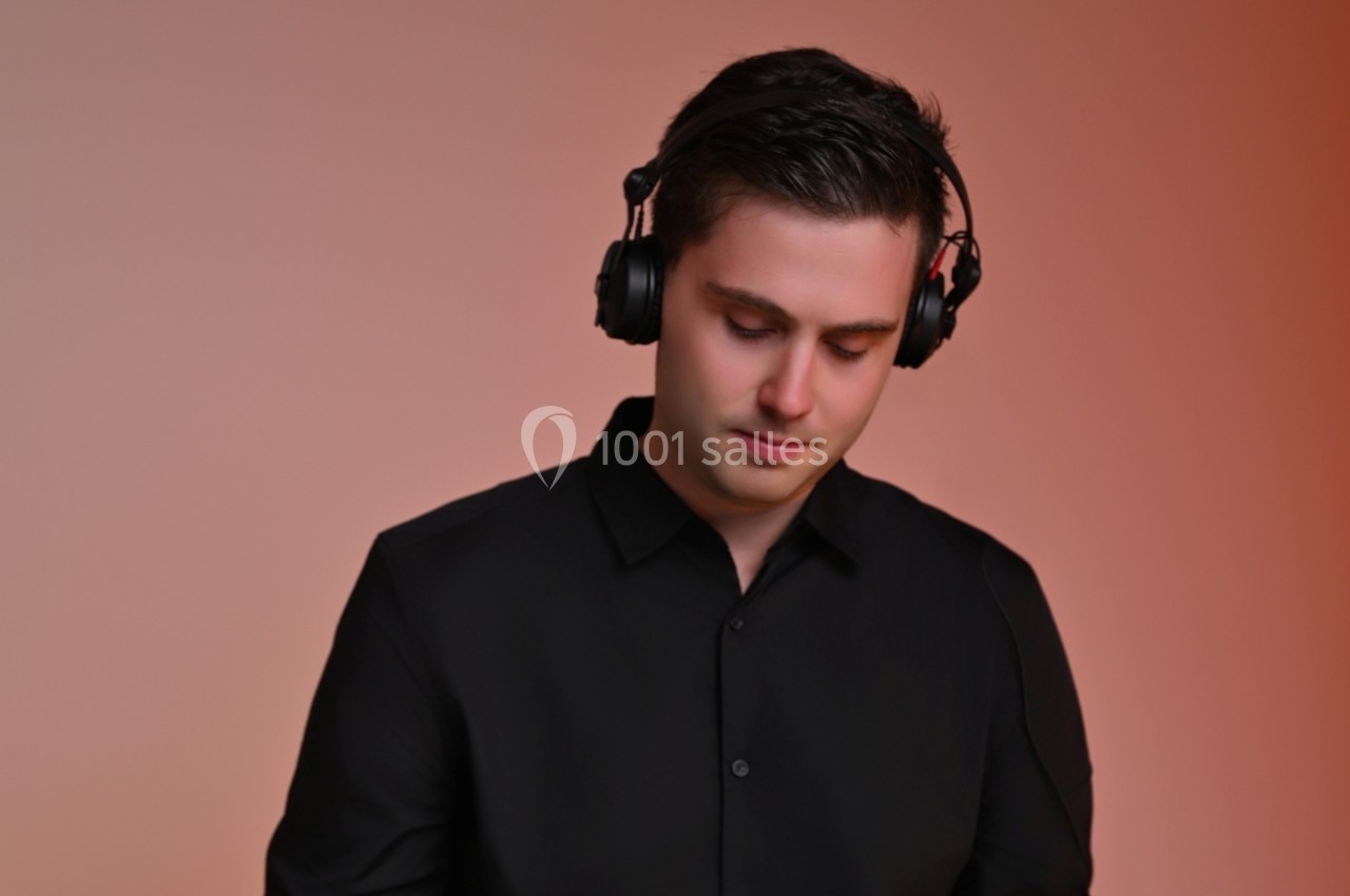 Un homme portant un casque audio noir regarde vers le bas, sur un fond dégradé orange.