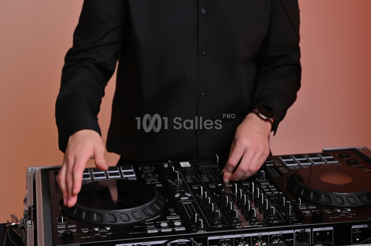 Personne en chemise noire utilisant une table de mixage DJ avec des platines et des commandes.